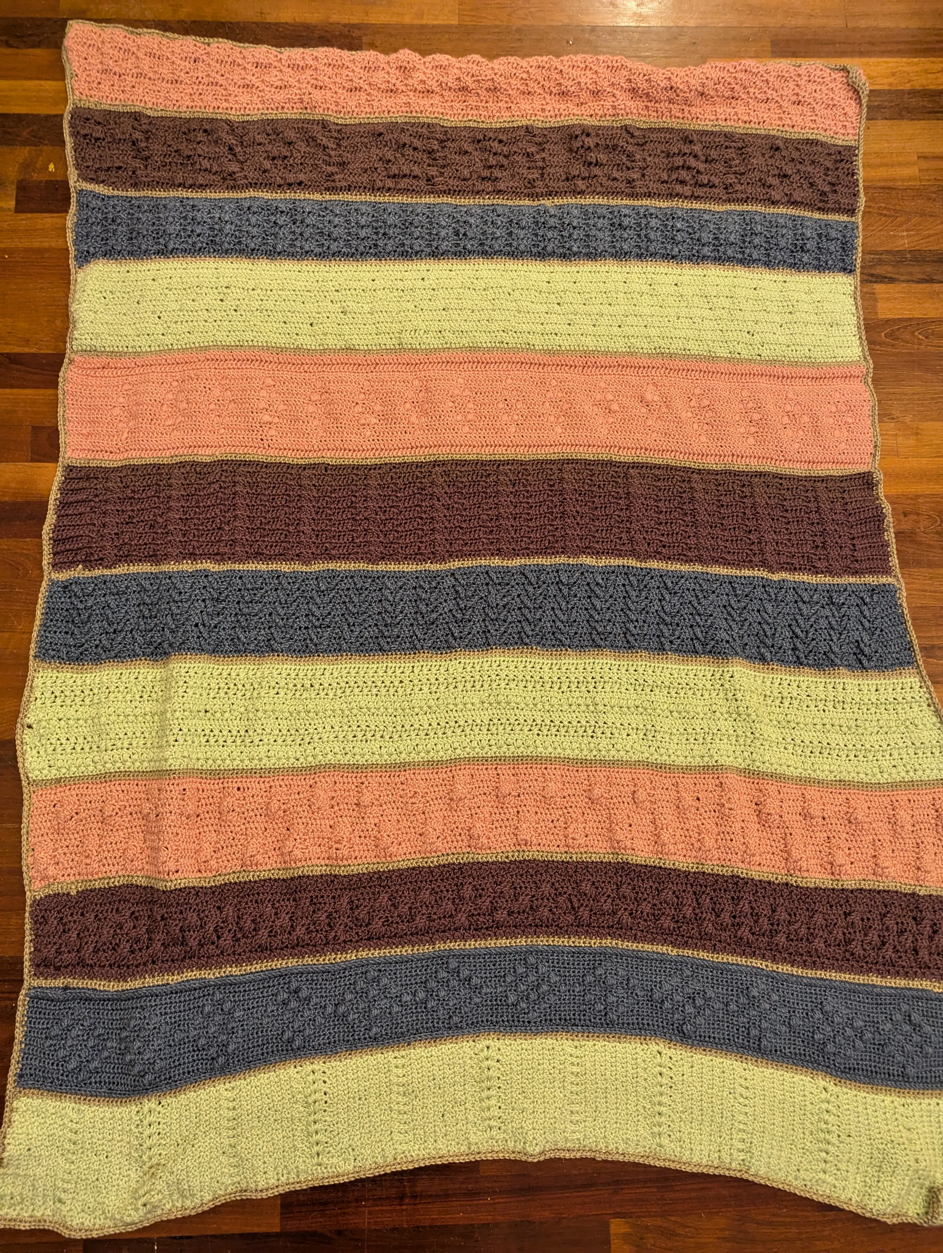 A green, blue, purple, and pink striped crocheted blanket with 12 thick stripes