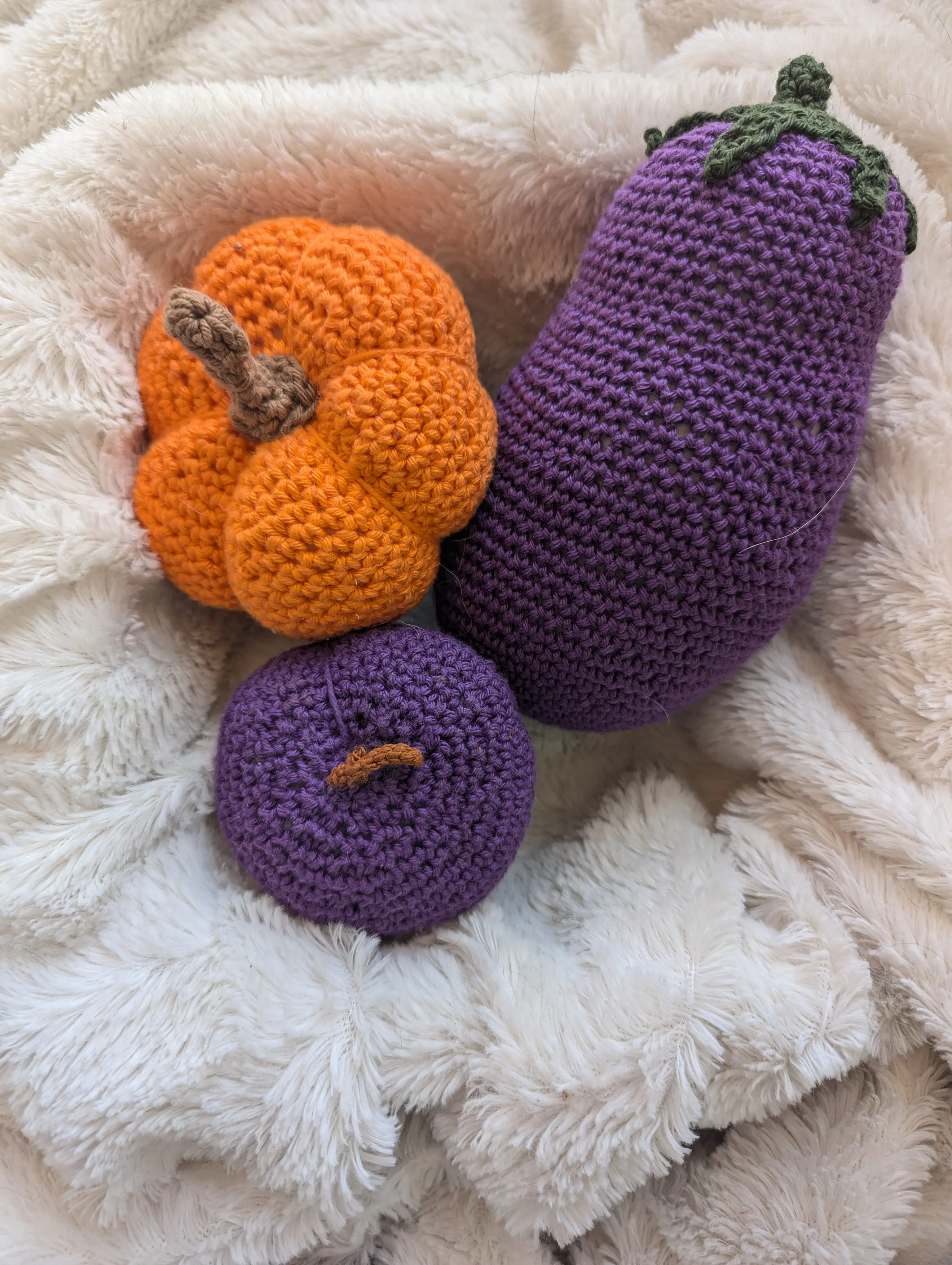 A basket with a crocheted eggplant, pumpkin, and plum